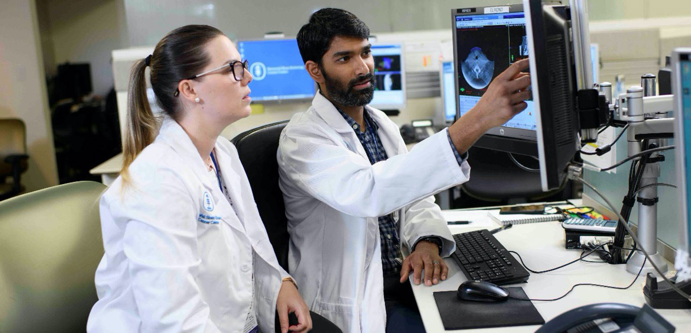 Two MSK Colleagues wearing lab coats looking at a computer monitor